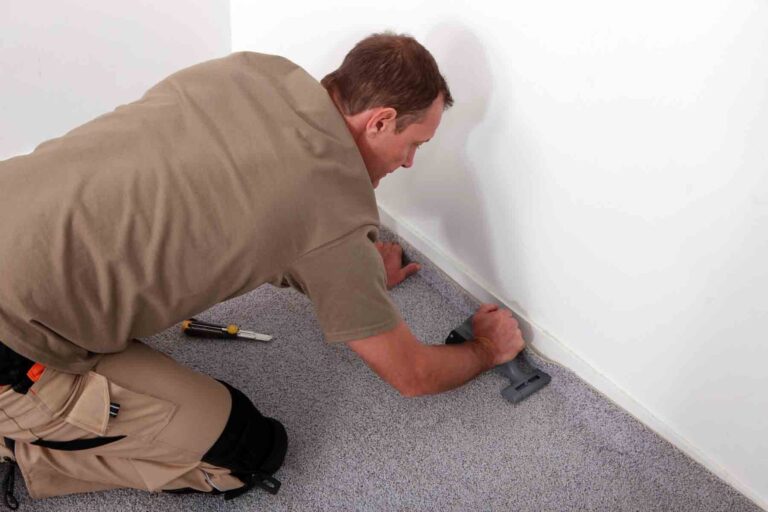 A man kneeling while installing carpet with tools